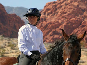 Woman trail riding against a backdrop of red rocks. She is wearing the Da Brim Rezzo helmet visor in black.