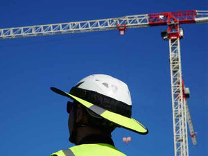 Construction worker Da Brim PRO Tech Lite Construction helmet visor brim in fluorescent yellow with reflective. Pictured with a crane.