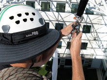 Load image into Gallery viewer, Da Brim PRO Tech Construction Helmet Visor Brim in gray at work. Man performing rigging duties at height while working and wearing the Da Brim PRO Tech Construction Helmet Visor Brim in gray.
